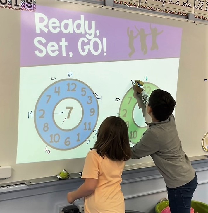 Two Franklin 4th graders write multiplication facts on interactive white board