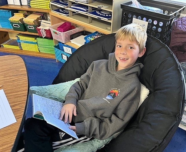 Jefferson 3rd grader sits in cushioned chair with book
