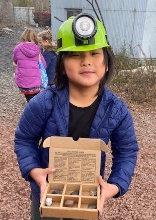 Franklin 4th  grader wears hard hat while holding box of rocks at Sterling Mines.