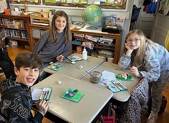 Three McKinley 5th graders smile for the camera as they paint clay landscapes in art