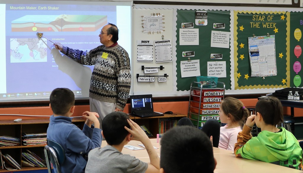 Tamaques parent points at presentation on screen while students at desk listen