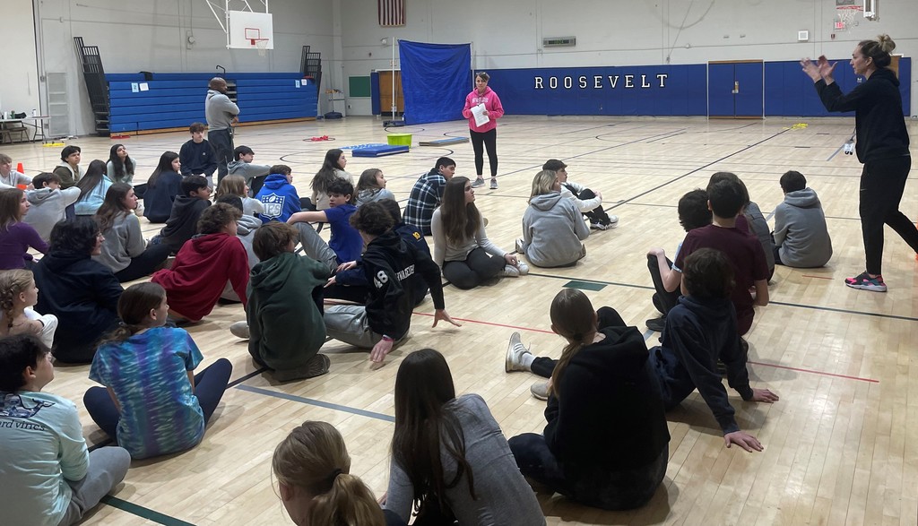 Students sit on gym floor as teachers goes over SEL activity