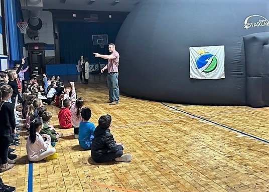 Students sit on floor near the traveling planetarium