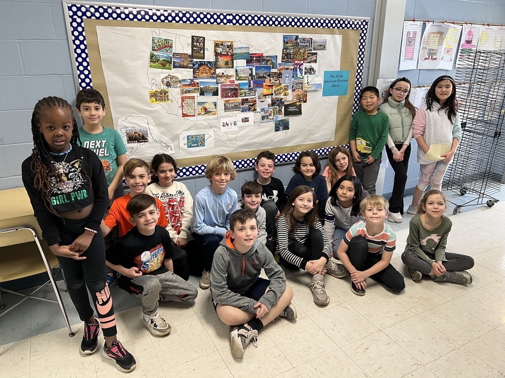 Group of 3rd graders stand in front of bulletin board with postcards