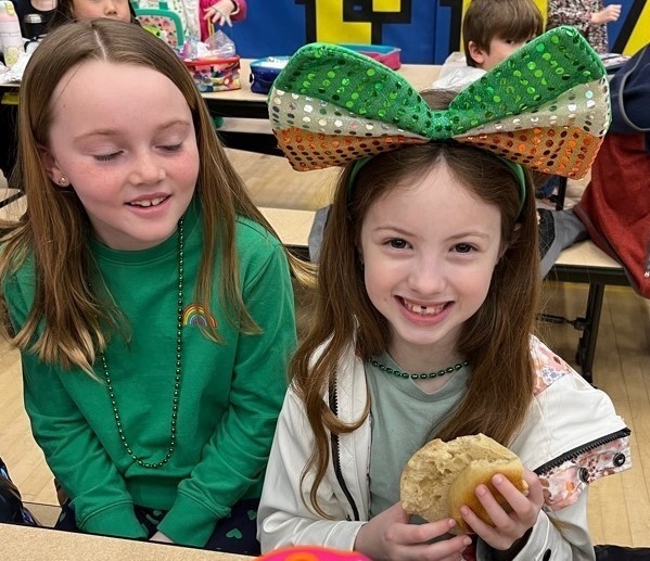 Two girsl in green, with one student wearing big green bow