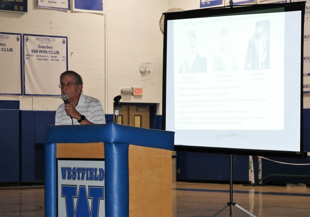 Ara Jeknavorian stands at podium in front of presentation screen, speaking to 9th grade assembly on the Armenian Genocide