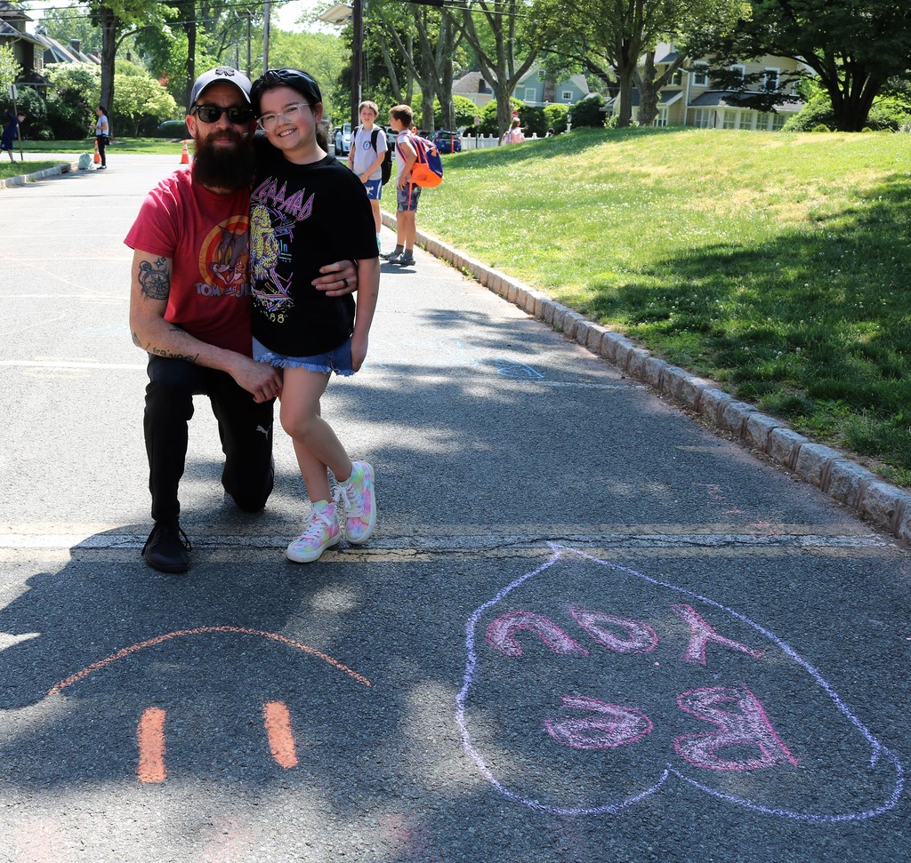 Father and daughter pose for a picture as they chalk a nice message and picture on school driveway